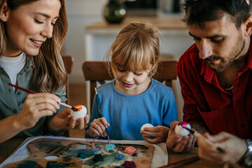 Family laughter as they enjoy decorating eggs with brushes and stickers for Easter celebration