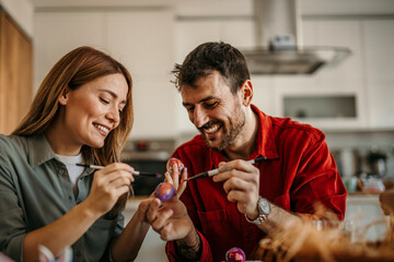 Loving couple collaborate and smile to create beautiful Easter egg designs at home.
