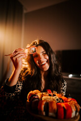 Naklejka premium Woman in pajamas joyfully enjoying sushi in bed under warm light with a vibrant sushi platter