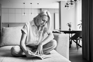 Woman sitting comfortably on couch, deeply engaged in reading book. Cozy living space with modern...