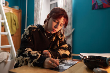 Medium shot of creative young female student wearing y2k outfit sitting at table, drawing picture of woman