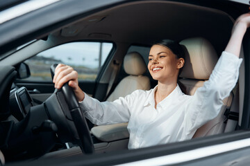 Car, driver, woman a woman sits in the driver's seat of a car with her arms raised and hands gripping the steering wheel, conveying a moment of excitement or celebration while driving