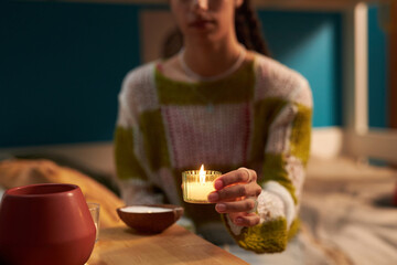 Biracial gen Z girl creating cozy and warm atmosphere in dorm room, lighting up scented candles
