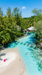 Crystal-clear waters meet soft sand on Koh Kood, Thailand, where visitors relax under the sun. Lush greenery and wooden walkways create a serene atmosphere for a perfect getaway.