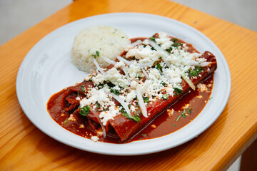 Traditional enchiladas with Oaxaca cheese, red mole and rice. Enchiladas are a dish from Mexican cuisine made with rolled or folded corn tortillas.