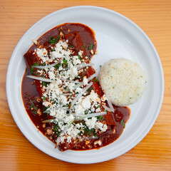 Traditional enchiladas with Oaxaca cheese, red mole and rice. Enchiladas are a dish from Mexican cuisine made with rolled or folded corn tortillas.