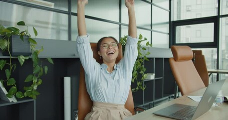 smiling young professional woman in glasses sitting in a modern office space with stylish leather chairs, plants, and natural lighting, looking confident and approachable