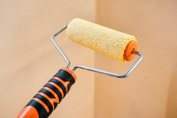 Fototapeta premium A paint roller with orange handle and yellow paint roller head, ready for painting.