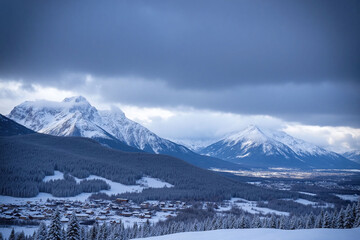 Rolling snow   covered terrain with forests, buildings and mountains