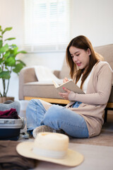 Asian woman planning her travel at home, ticking off a detailed packing list as she packs travel essentials into her suitcase.woman organizing everything she needs for a successful trip.