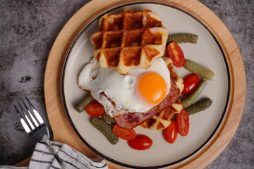 Breakfast waffles with fried eggs Tomatoes and pickled cucumbers In a white plate with a black background