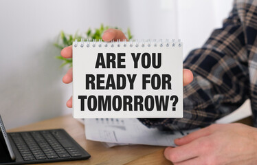 A person holding a spiral bound notebook with the words Are You Ready For Tomorrow written on it.