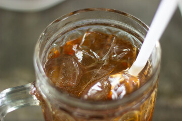 A glass filled with iced tea, clear ice cubes, and a white straw for drinking