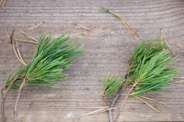 
A wooden board with two pine branches on it.  The branches have long, needle-like needles that are bright green in color. A few fallen needles are scattered around the branches.