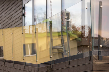 Balcony enclosed by glass balcony railings. The floor of the balcony is made of wood, and behind the glass railing you can see elements of another building or structure.