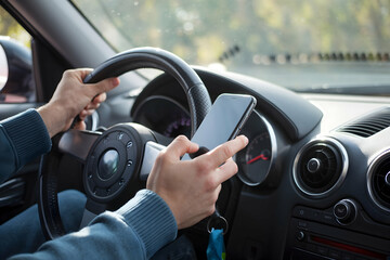 Car interior with focused driver, holding phone and steering wheel