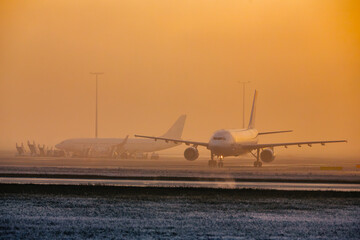 Traffic at airport in dense fog at dusk. Wide shot of airplanes on frosty winter day..