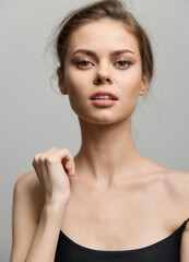 Elegant young woman with natural makeup posing confidently against a soft gray background. Beauty and self-expression concept.