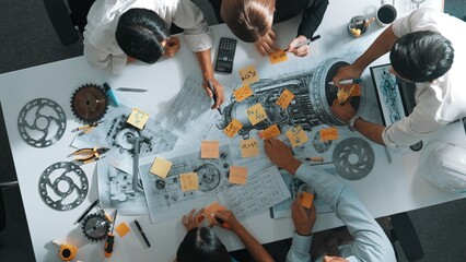 Top view of smart engineer team in casual cloth talking about turbine engine structure at table with metal gear, calculator, sticky notes. Group of technician taking a note in meeting. Alimentation.