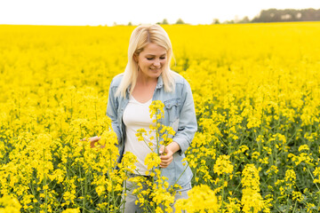 Fototapeta premium Portrait of attractive woman on blooming rapeseed field with sunset light. Yellow flowers and happy woman