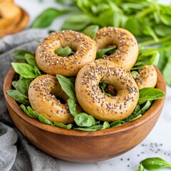 Bowl filled with mini sesame bagels arranged with fresh spinach leaves, emphasizing wholesome snacking and creative bread presentation