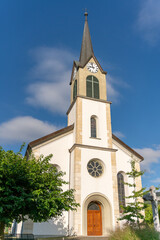 Rural little, but beautiful church behind some trees, and under a blue, slightly clouded sky. Vertical photograph.