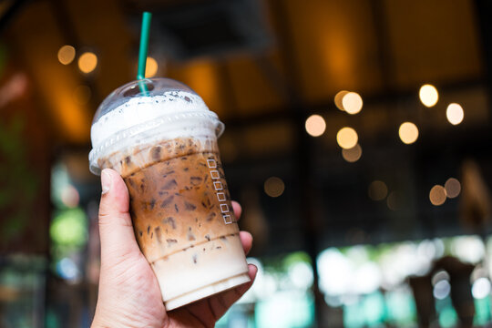 Someone hand holding a plastic cup of iced Mocha coffee and. Ready to go package. Favorite caffeine beverage manu
