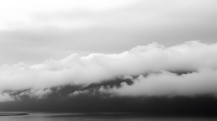 Fototapeta premium A serene black and white landscape featuring a lake, mountains shrouded in thick, atmospheric clouds, and a muted palette