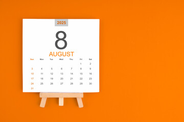 Naklejka premium Calendar page for August 2025 with wood easel on orange background.