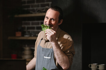 Portrait of a man in the kitchen. He is preparing a vegetarian salad, chewing a green leaf.