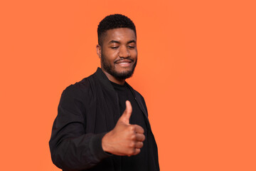 Man giving a thumbs up against a bright orange background while smiling confidently
