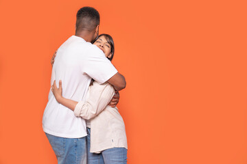 Couple sharing a warm embrace against an orange background in a cozy indoor setting