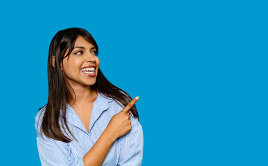 Smiling woman pointing to the side with enthusiasm in a vibrant blue backdrop