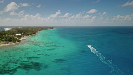 Aerial view motorboat sails vibrant turquoise water lagoon along tropical island atoll coast. White speedboat cruise south pacific ocean in sunny day. Remote wild nature paradise, exotic summer travel