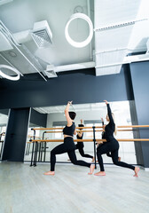 Women practicing dance in modern studio. Two women engage in a dance practice session in a sleek and contemporary studio with mirrors and wooden bars.