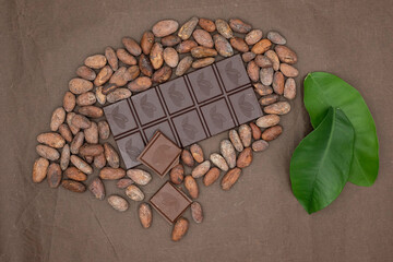 Cocoa fruit is designed from chocolate bars and cocoa beans. Chocolate color tissue paper background. Green leaves. Chocolate production concept.