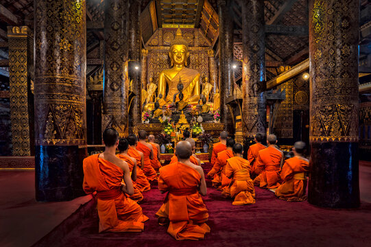 Monk Praying in Wat Xieng Thong temple with blue sky, Luang Prabang, Laos. Buddhism culture and religion	
