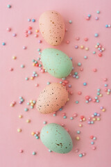 Colorful speckled eggs arranged on a pink background with small candy decorations for seasonal celebrations