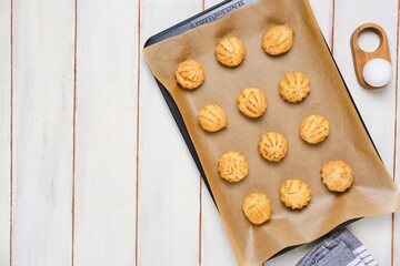 Baked choux pastry profiteroles on a baking sheet with baking paper on a white wooden background. The process of making choux pastry products.