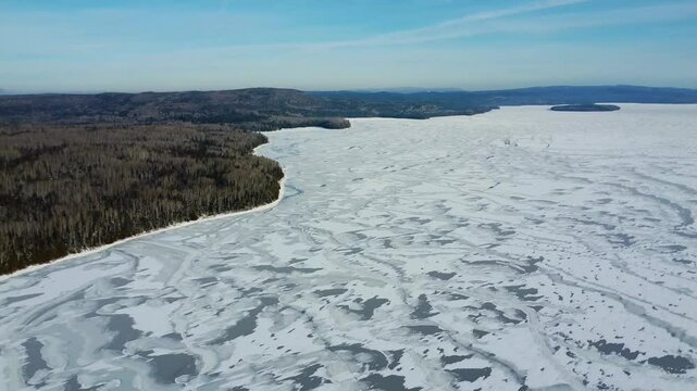 Aerial winter panorama over the vast frozen surface of Lake Matapedia, showcasing natural ice patterns, snow-covered wilderness and forested landscapes in the Matapedia Valley, Quebec, Canada.