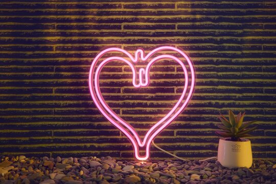 Glowing pink heart neon light on pebbled surface with small potted plant. - Powered by Adobe