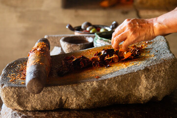 Woman from an indigenous community in Oaxaca preparing traditional red mole with a metate, a tool for grinding ingredients in Mexico.