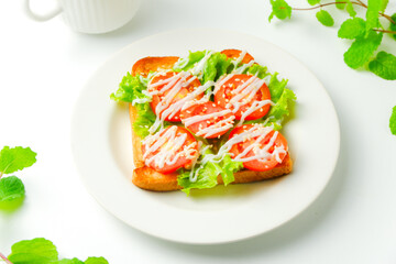 Colorful toast healthy sandwich with green lettuce and red tomato on a white plate, white mug and mint leaf for breakfast