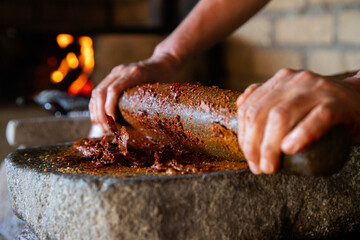 Woman from an indigenous community in Oaxaca preparing traditional red mole with a metate, a tool for grinding ingredients in Mexico.