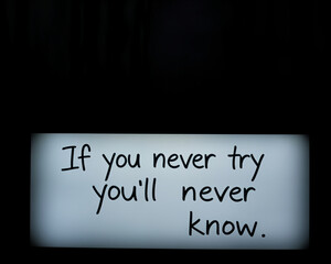Motivational quote about trying new things displayed on a lightbox. A close-up of a lightbox displaying a handwritten motivational quote, "If you never try you'll never know." The setting is dark.