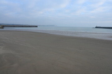sandy low tide view of Newhaven harbour walls with Seaford head in the distance