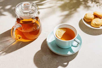 Cup of fresh tea and  teapot on a sunlit table.