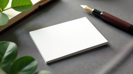 Blank business cards rest on a textured surface beside an elegant fountain pen and a spiral notebook