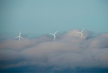 three wind turbines with clouds below and blue sky on top