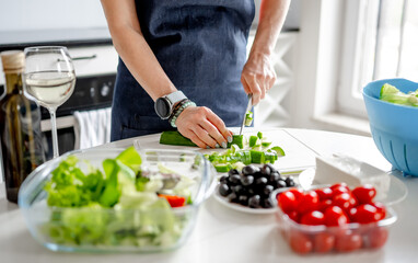 Woman At Home In Kitchen Cuts Cucumbers Preparing Greek Salad